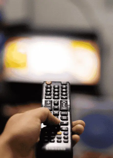 Hand holding a TV remote pointed at a screen, representing common issues that require TV repair.